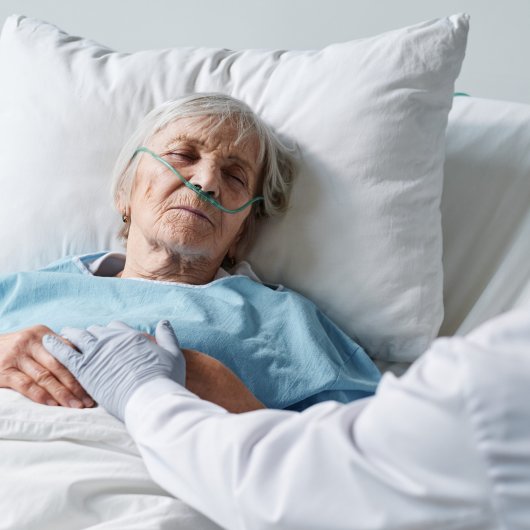 Dame âgée en fin de vie allongée dans son lit d'hôpital et se faisant réconforter par le médecin.