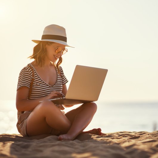 Female traveler sitting on the beach and working on her laptop.