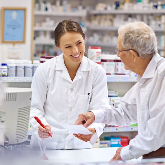 Female pharmacist giving advice to an elderly man standing across the counter.