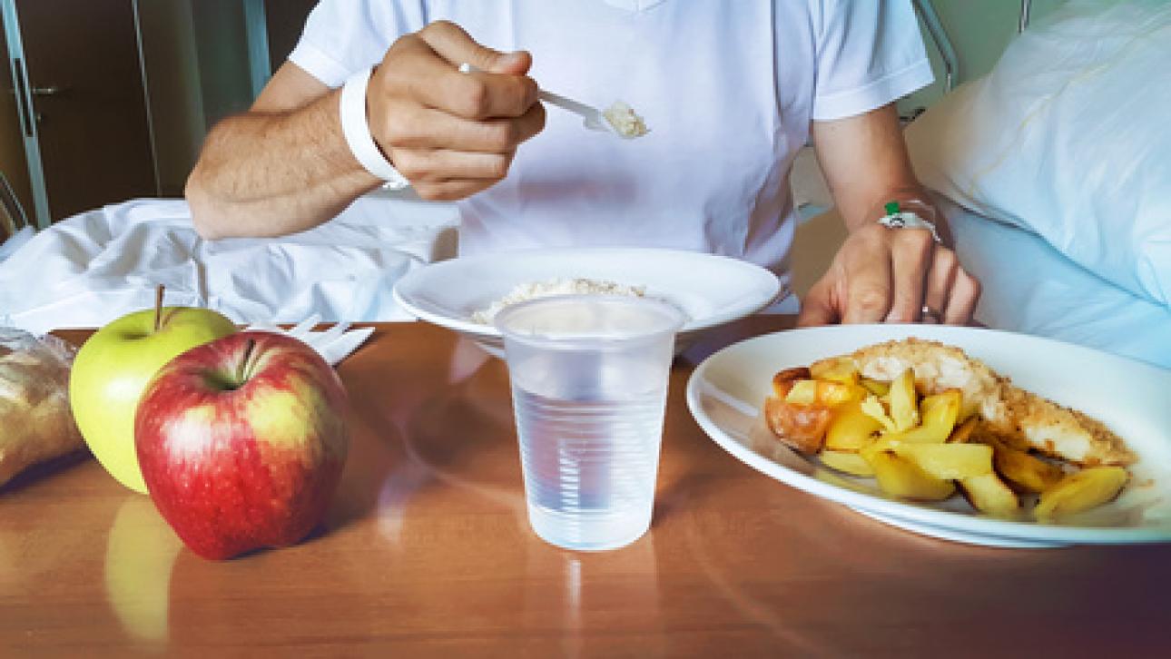 Homme assis dans un lit d'hôpital et mangeant un repas