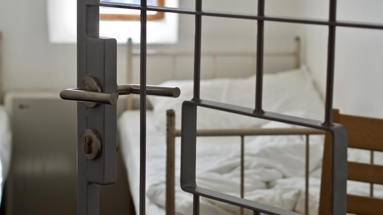 Lit vu à travers la porte à barreaux d'une cellule de prison
