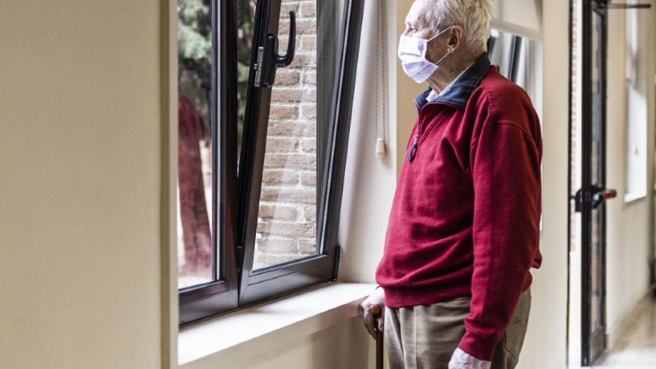 Elderly wearing a mask and looking out the window