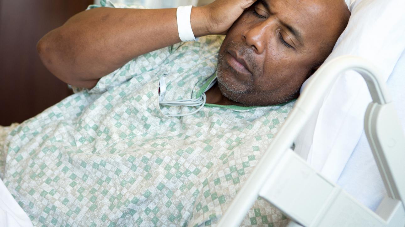 Homme se tenant la tête dans son lit d'hôpital