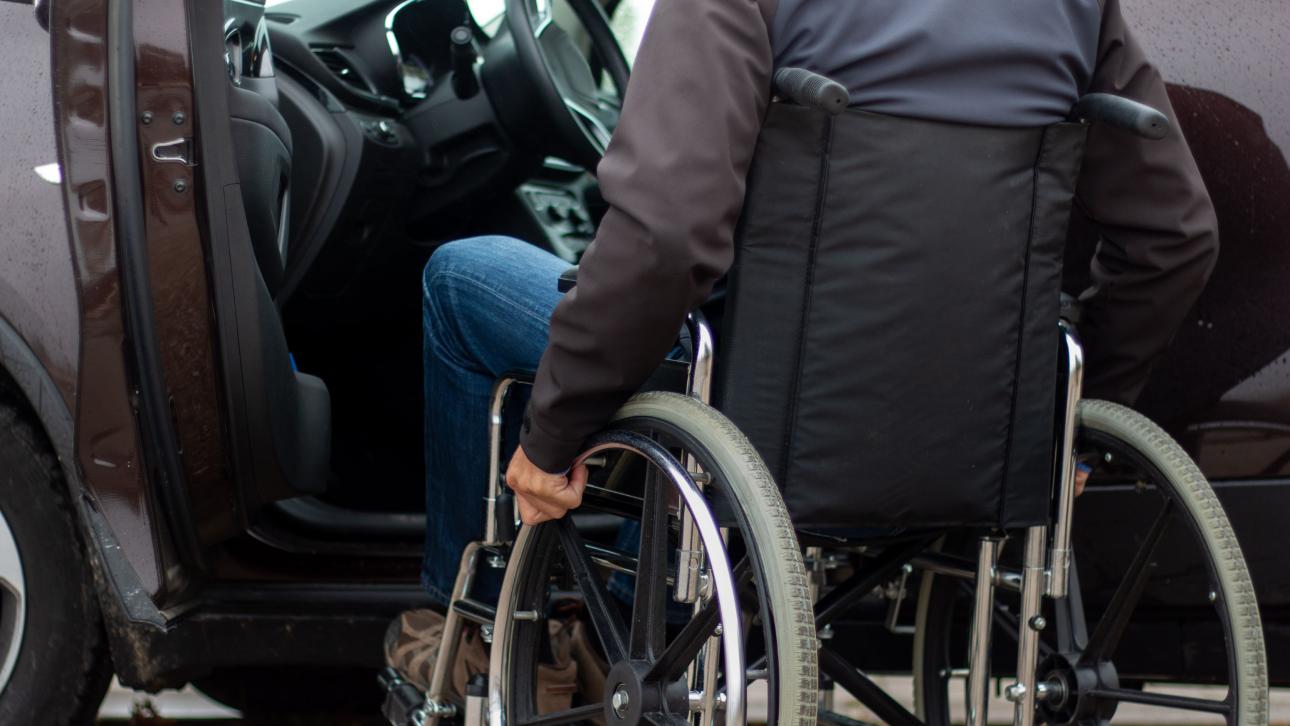 Homme en fauteuil roulant devant la porte ouverte d'une voiture