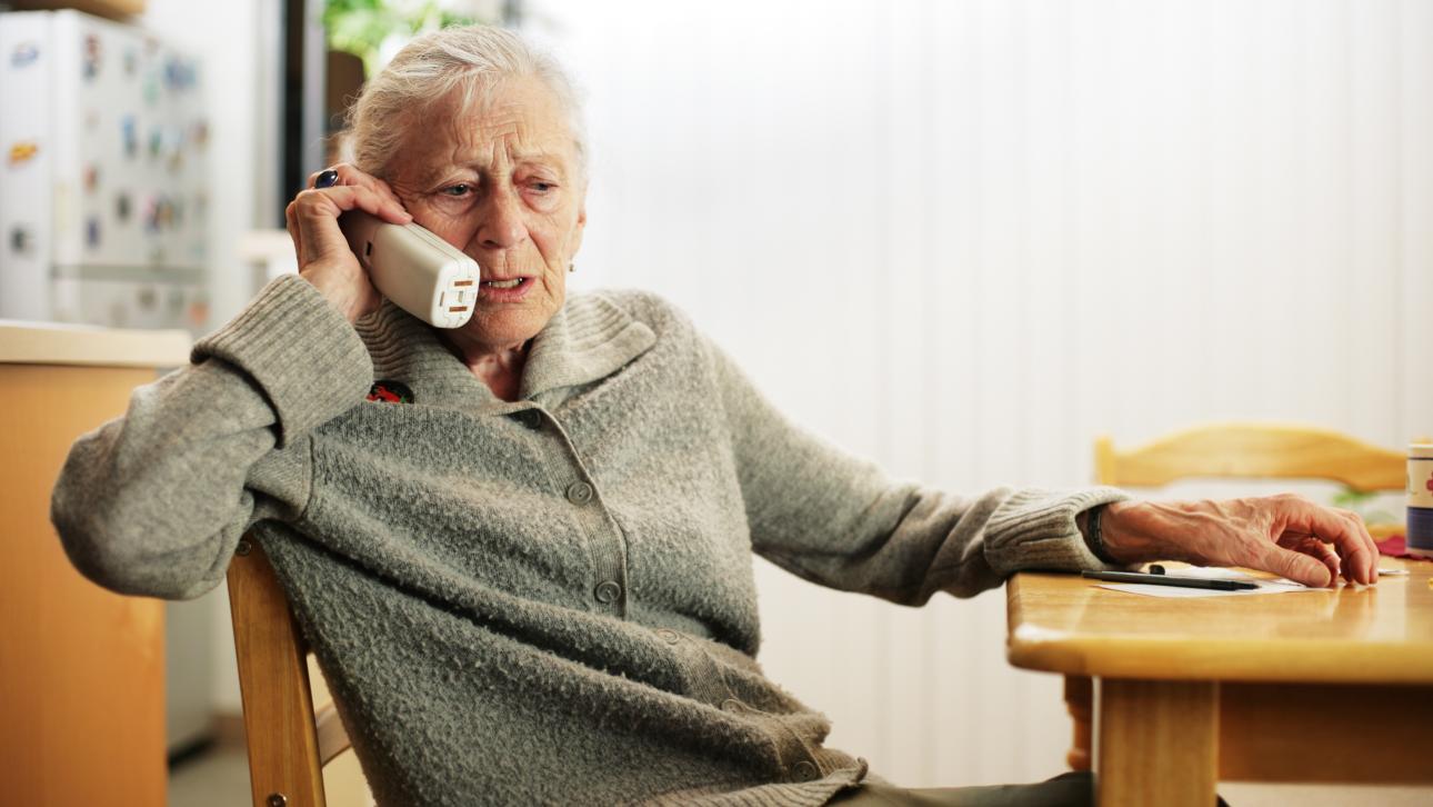 Dame âgée assise sur une chaise et parlant au téléphone