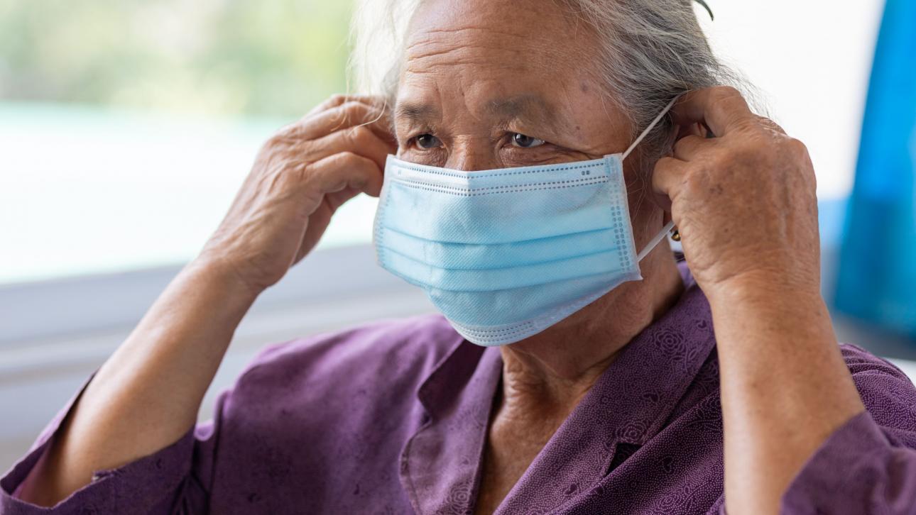 Femme âgée enfilant un masque jetable bleu