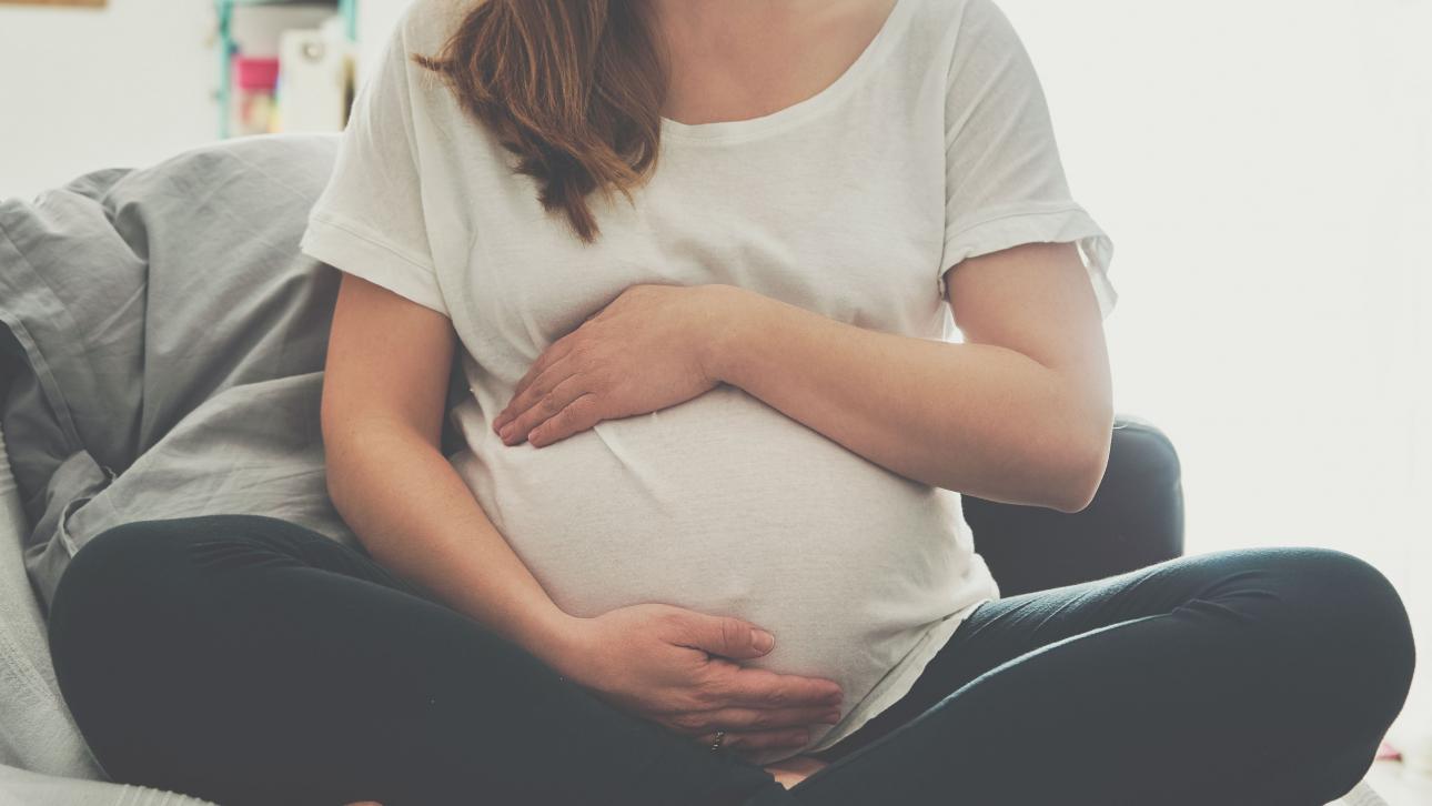 Femme enceinte assise sur un divan et tenant son ventre arrondi