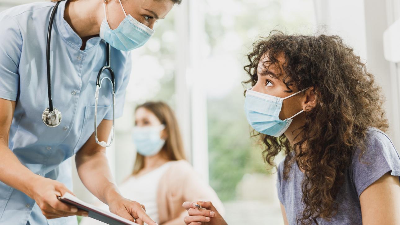 Jeune femme s'apprêtant à signer le formulaire que lui tend une infirmière