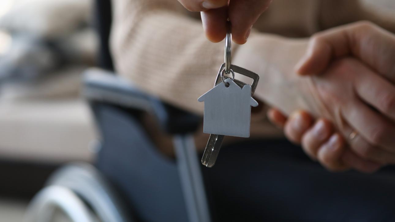Porte-clé en forme de maison tendu devant une personne en fauteuil roulant