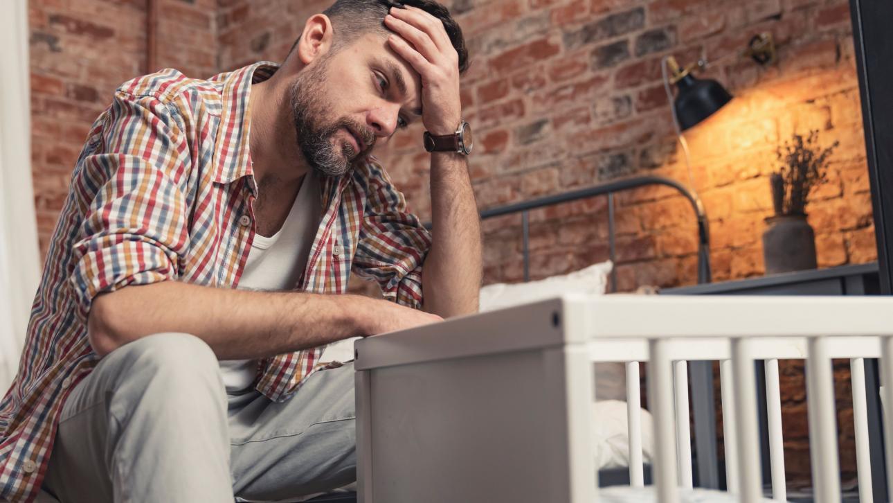 Père triste assis près d'un berceau