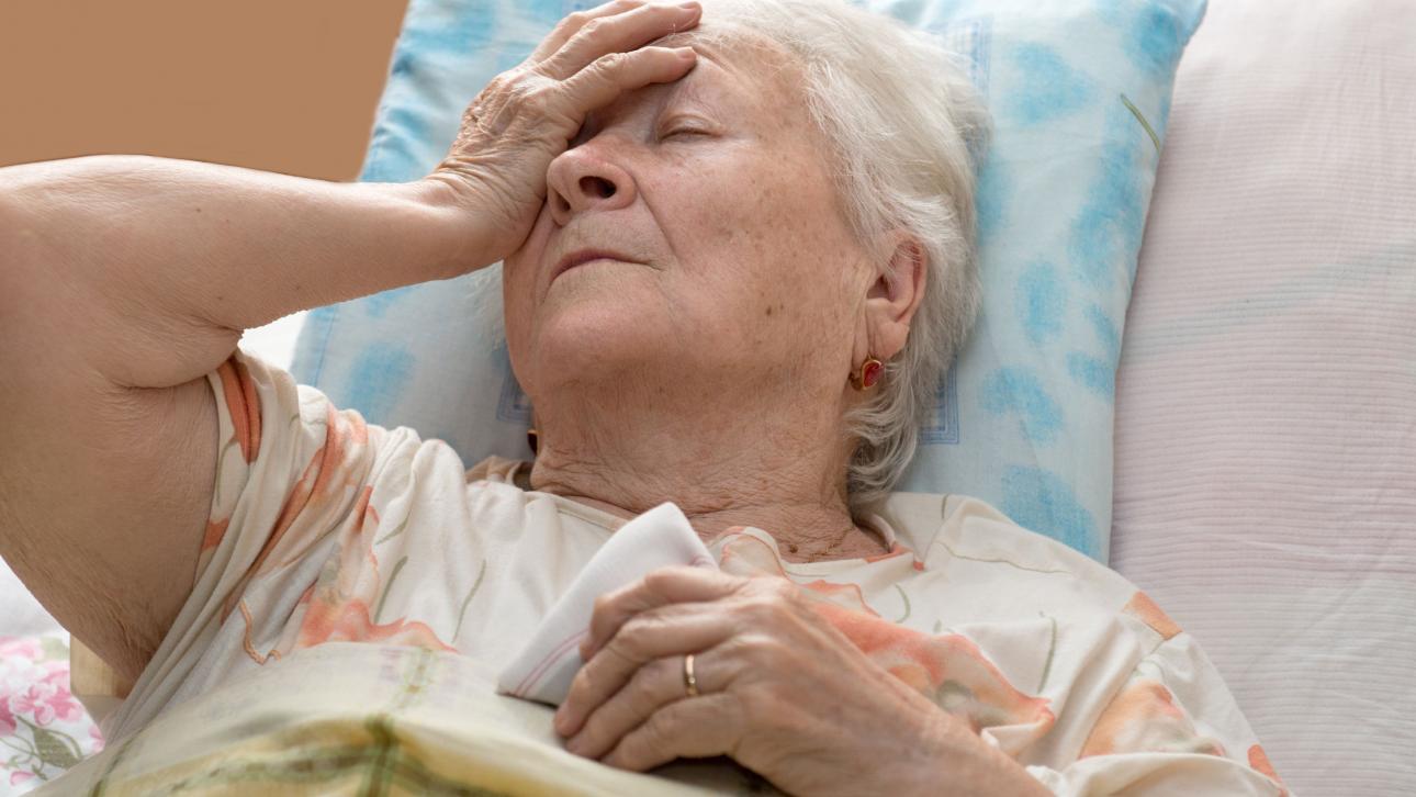 Dame âgée allongée dans un lit avec sa main sur son front