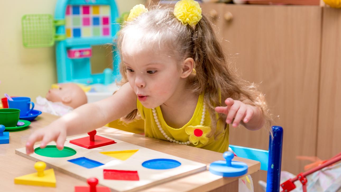 Fillette avec un handicap jouant à un jeu sur une table de la garderie