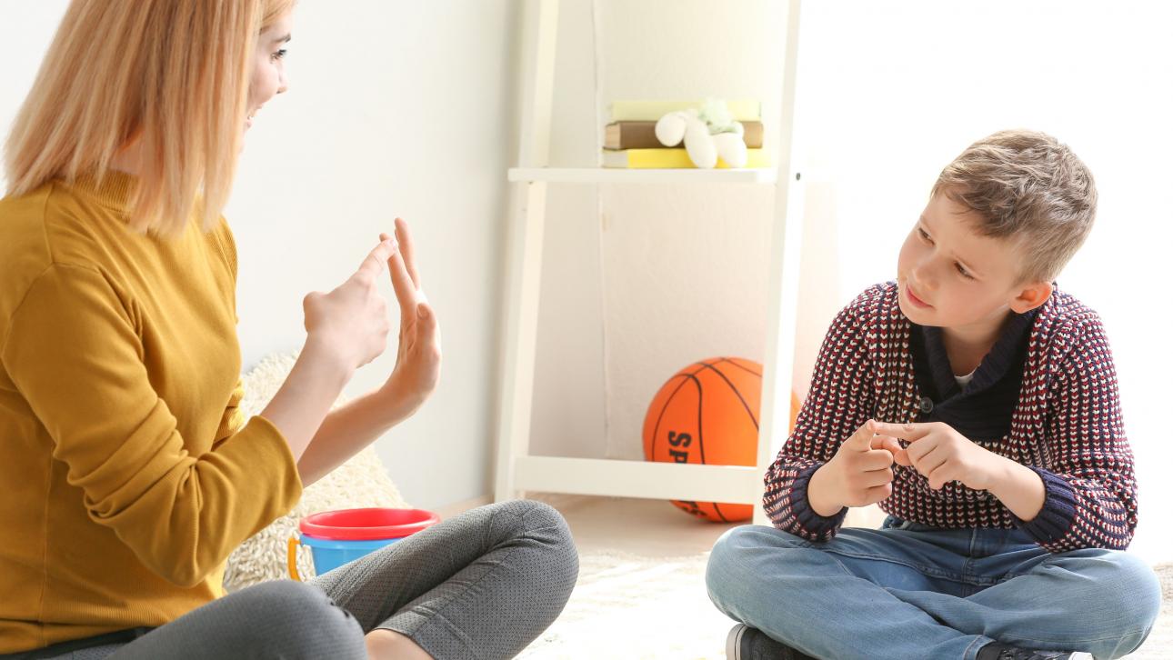 Female teacher showing fingers of her hand to a boy sitting on the floor