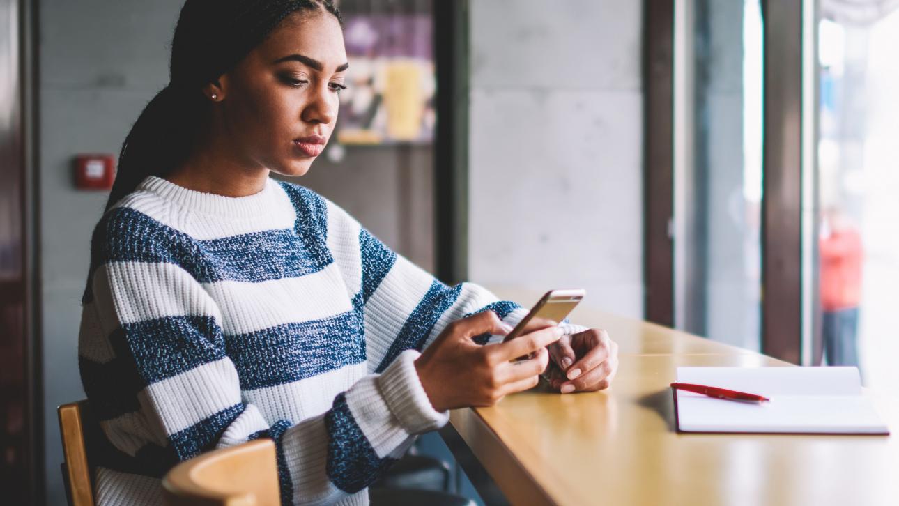 Étudiante regardant son cellulaire assise dans un café