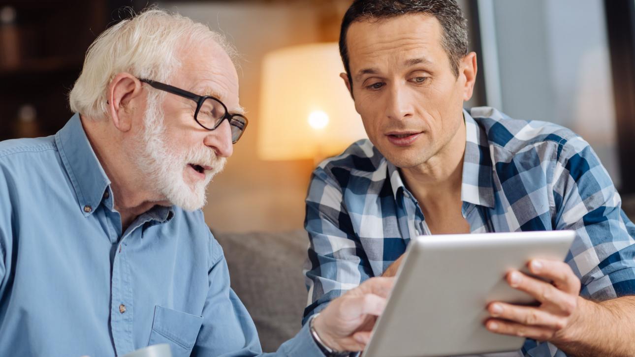 Un homme montre l'écran d'une tablette électronique à une personne âgée