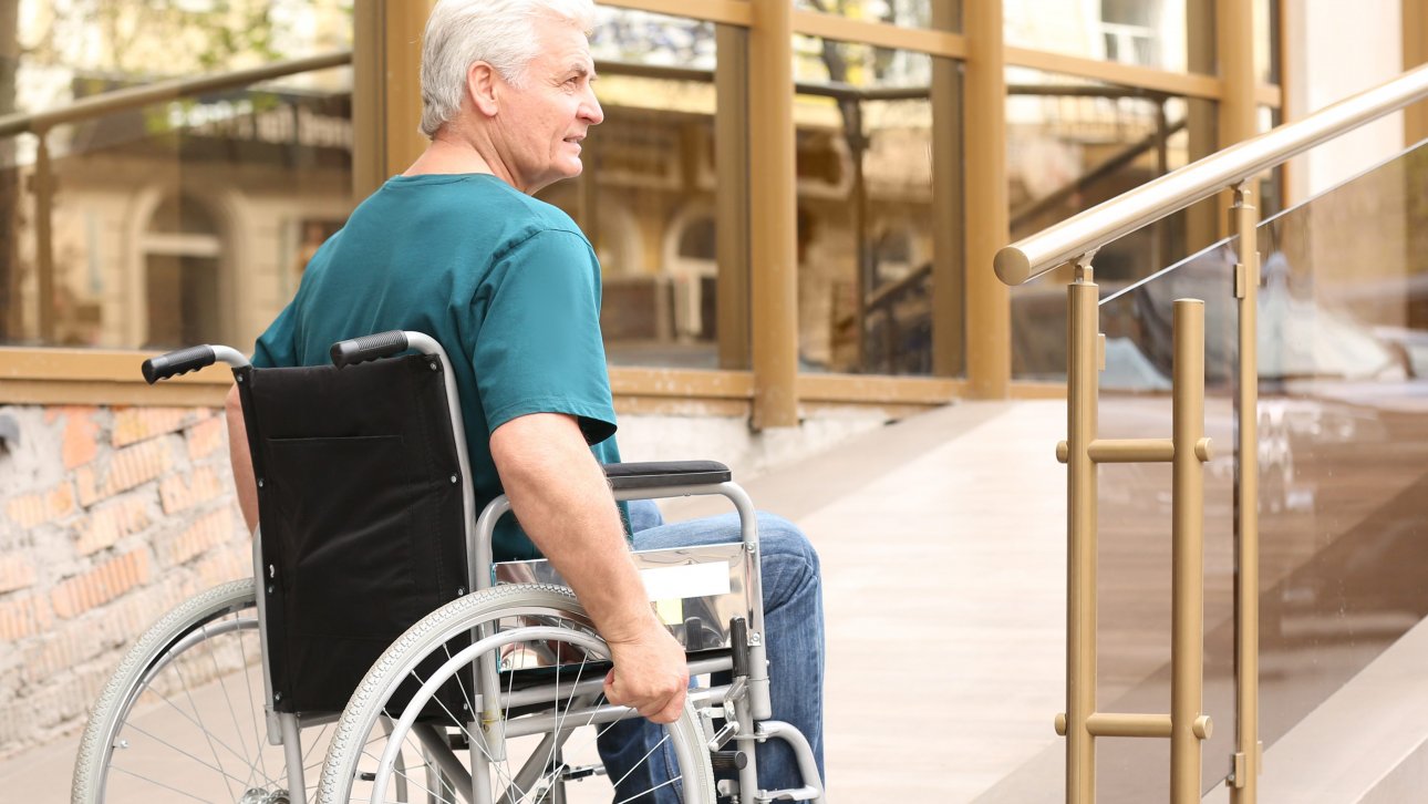 A man in a wheelchair in front of the access ramp to a private residence for seniors