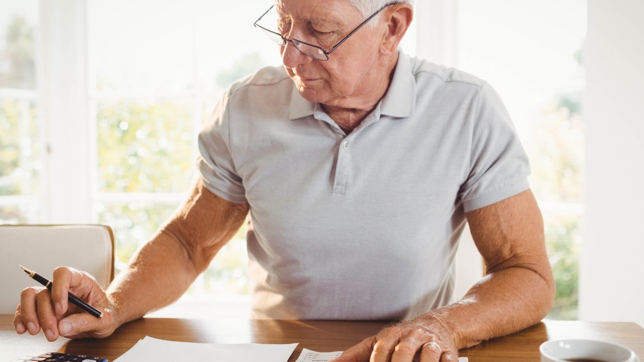 Homme aux cheveux blancs utilisant une calculatrice devant des documents papier