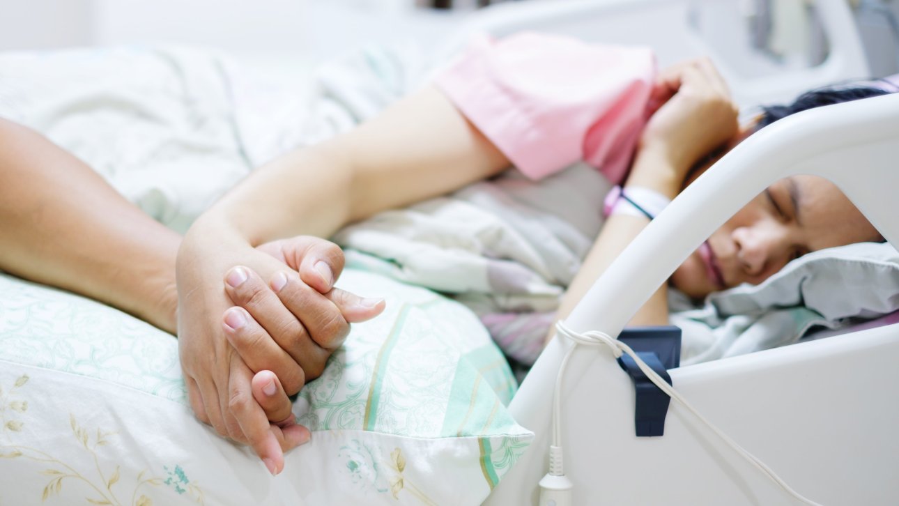 Woman lying in a hospital bed and holding her attendant's hand