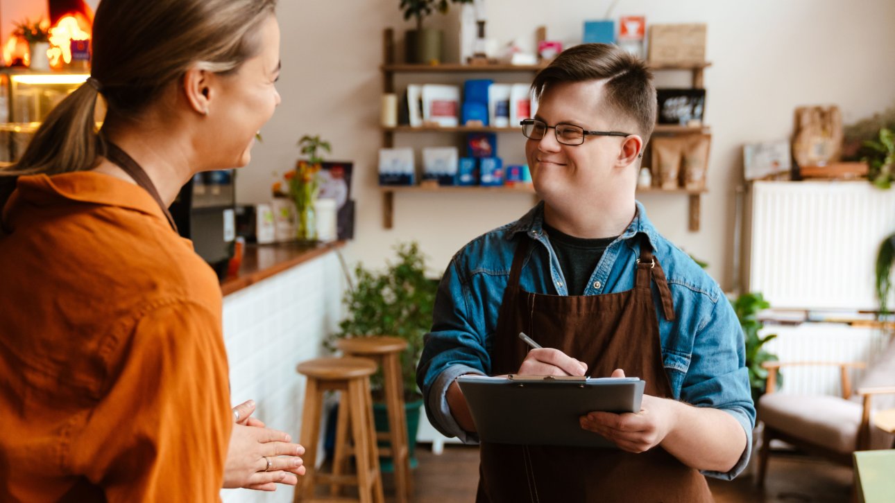 Young waiter with Down syndrome chatting with female colleague and taking notes