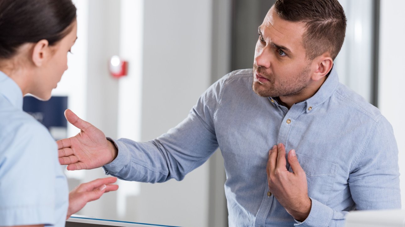 Dissatisfied man talking with the nurse who is behind the reception desk