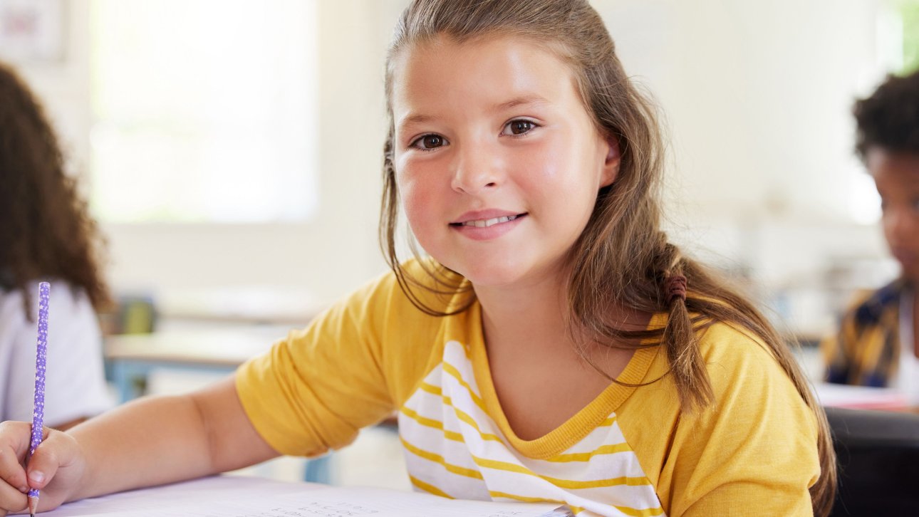 Jeune élève assise en classe et écrivant dans un cahier posé sur son bureau