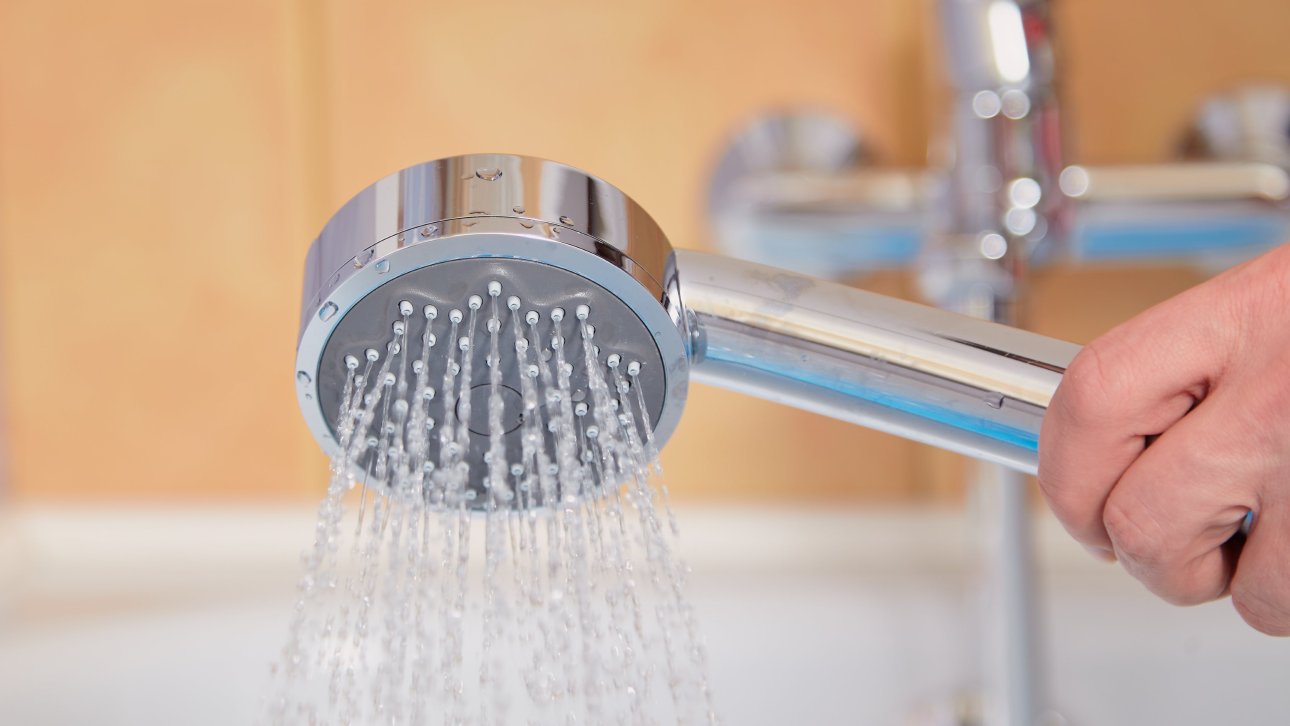 Hand holding a shower head with water flowing from it.