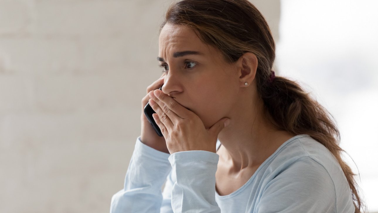 Woman putting a hand over her mouth and showing a surprised look while talking on the phone.