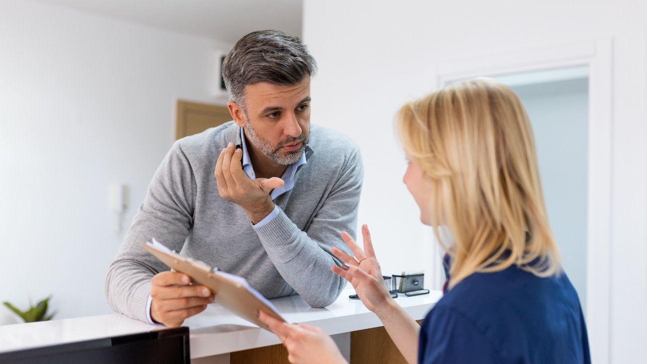 Man chatting with health clinic receptionist about a misunderstood bill.