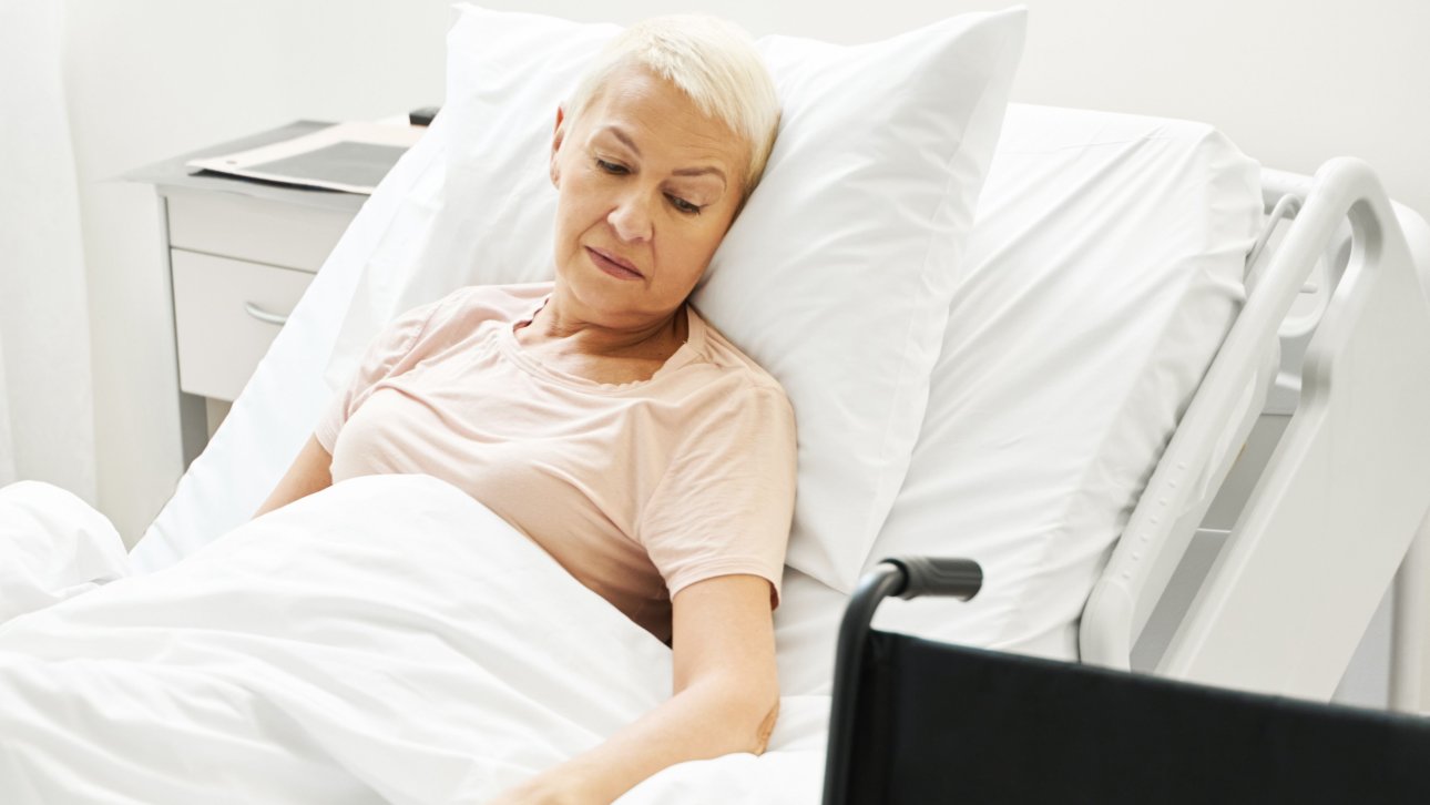 Bedridden patient in a CHSLD looking at the empty wheelchair placed next to her.