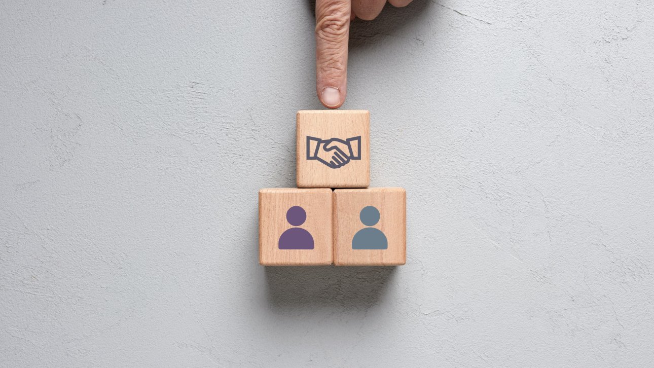 Two wooden blocks, each depicting a person, are placed under another block depicting a handshake.