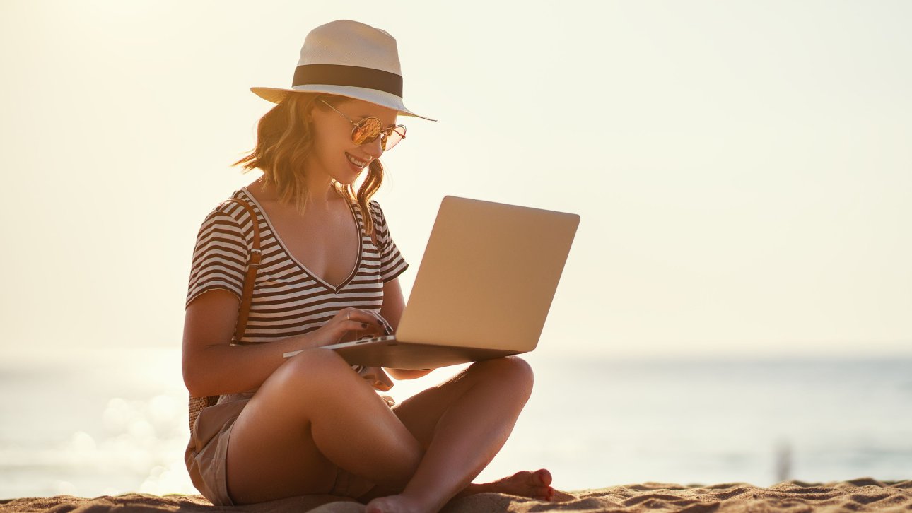 Female traveler sitting on the beach and working on her laptop.