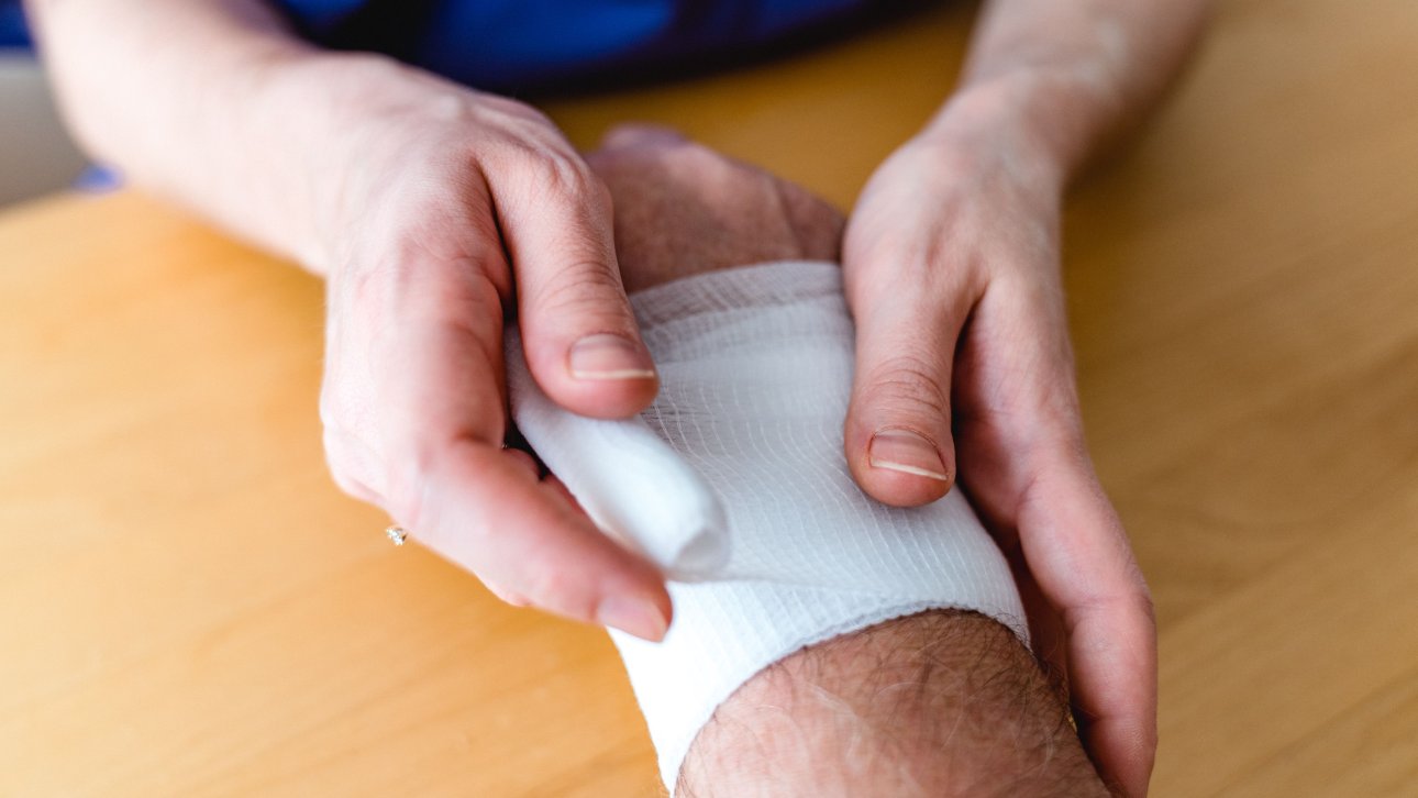 A person wrapping another person's wrist with a bandage.