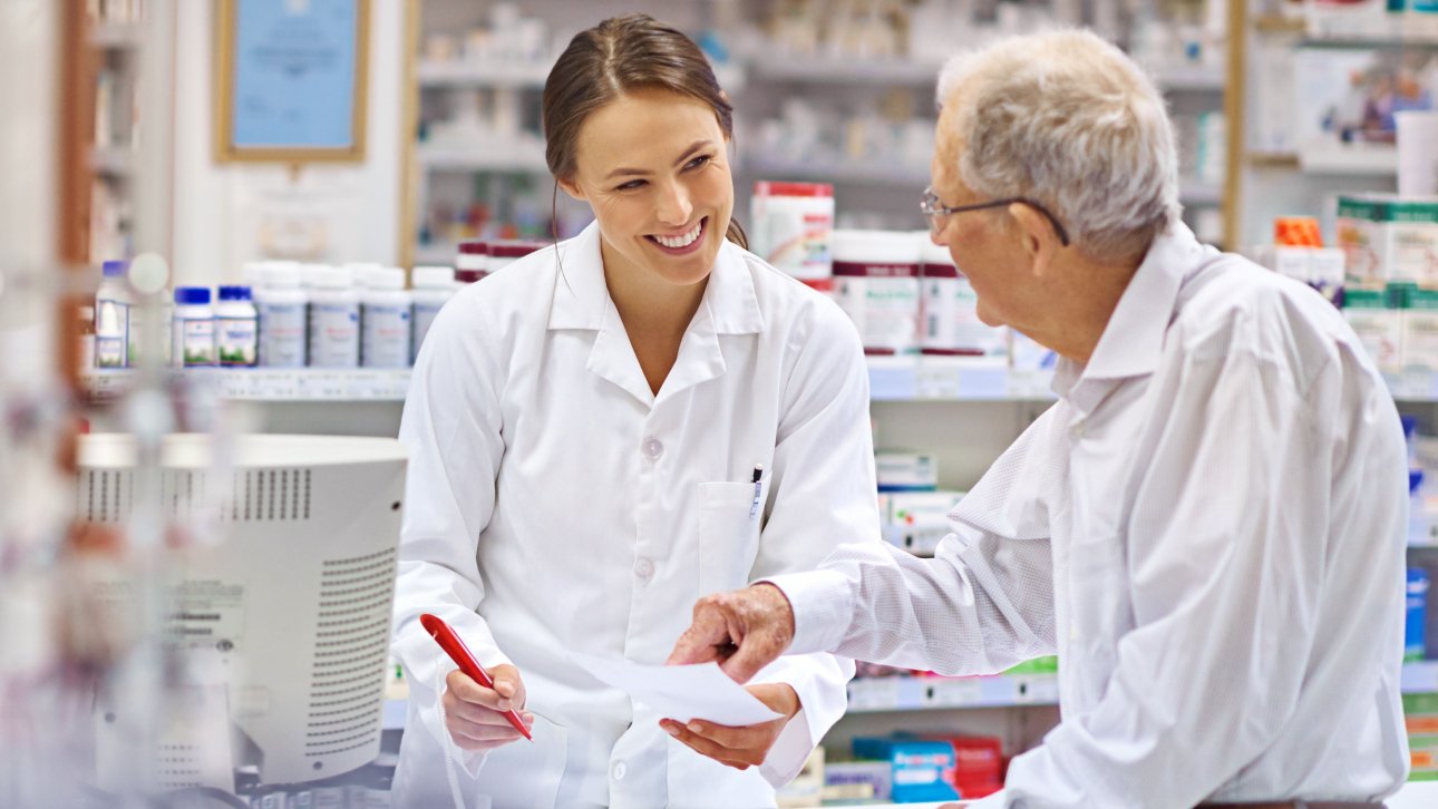 Female pharmacist giving advice to an elderly man standing across the counter.