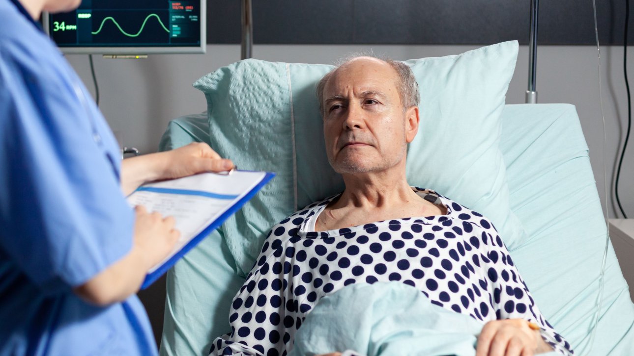 Man lying in a hospital bed and staring at a female officer who is holding a form.