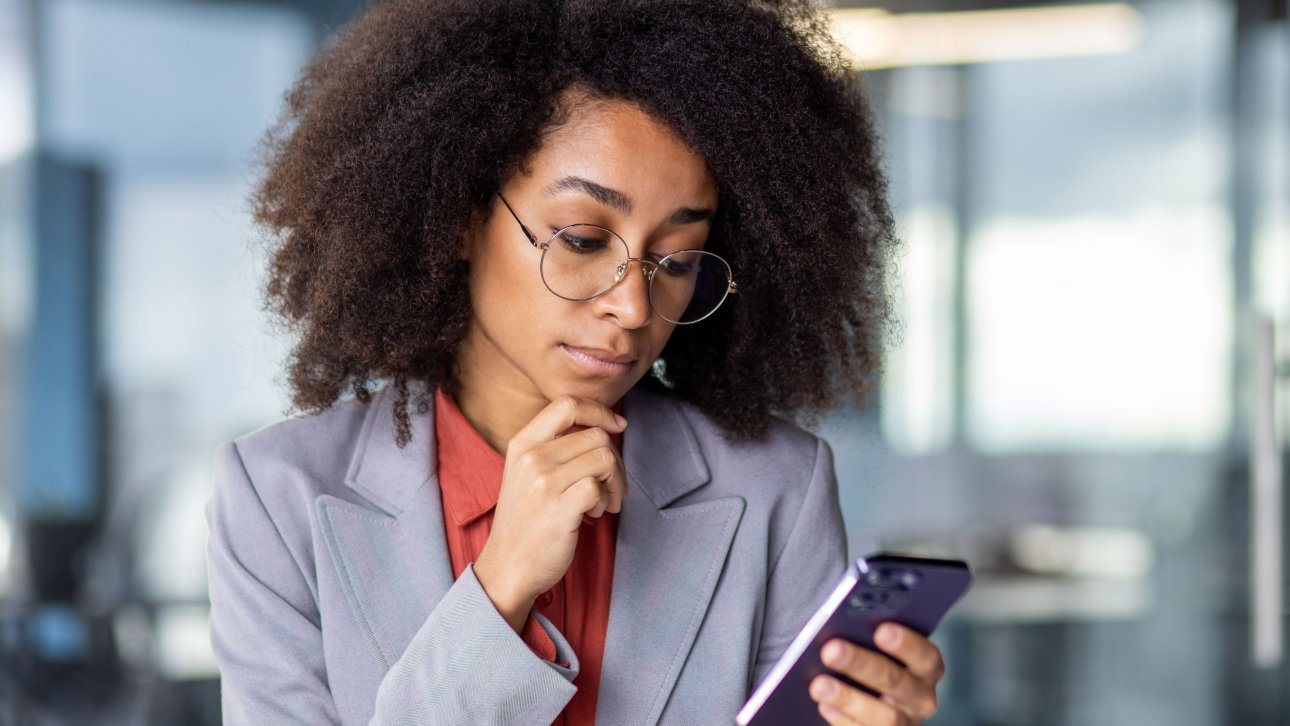 A professional employee looks doubtful while looking at her cell phone in the office.