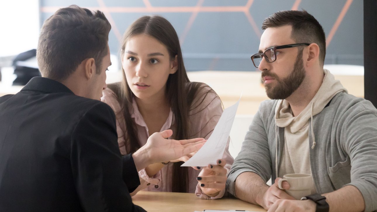 Sitting at a desk, a young couple argues with a lawyer.