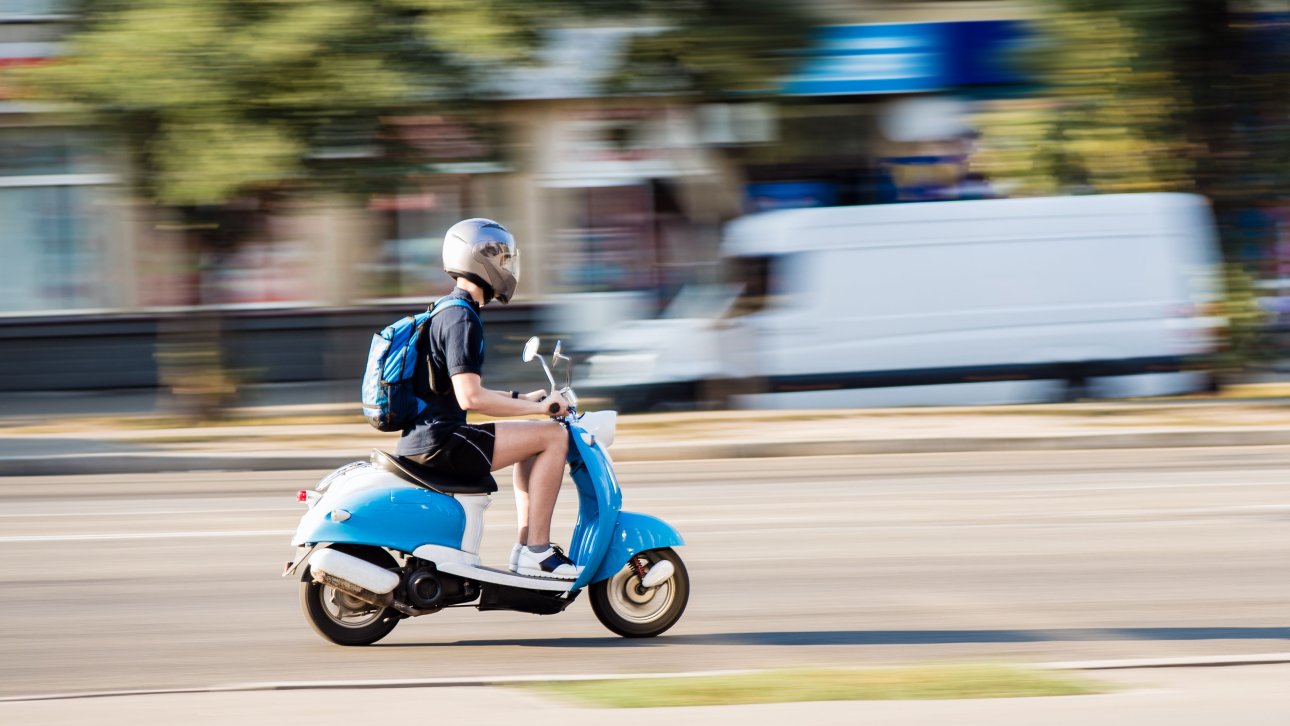 Adolescent conduisant un scooter sur la route.