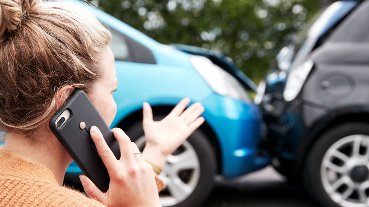 Victim of a road accident talking on cell phone while looking at her car which collided with another vehicle.