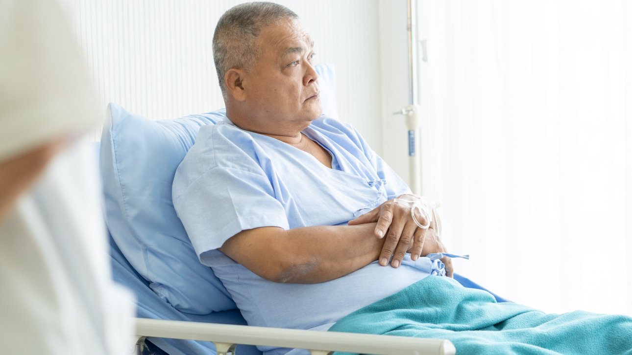 A man lying in his hospital bed looks displeased.