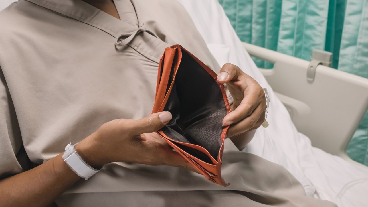 Patient couché sur un lit d'hôpital et montrant l'intérieur de son portefeuille vide.