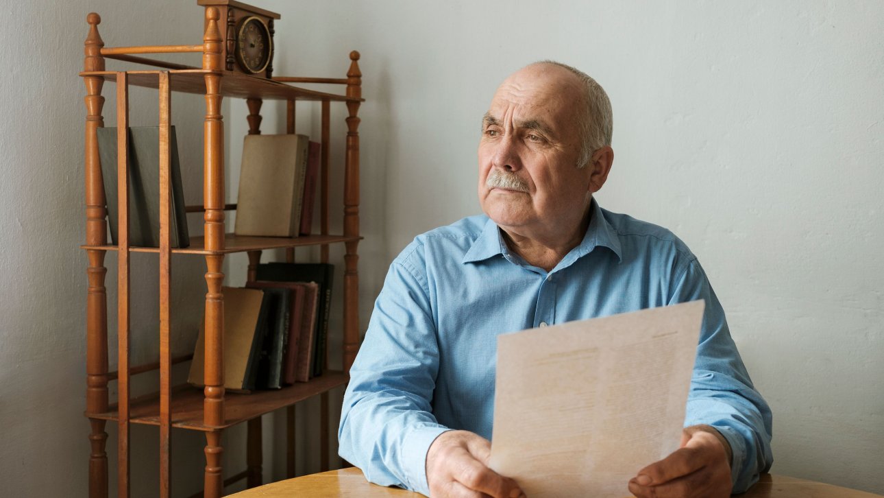 Un aîné tient un document dans ses mains en regardant au loin d'un air triste.