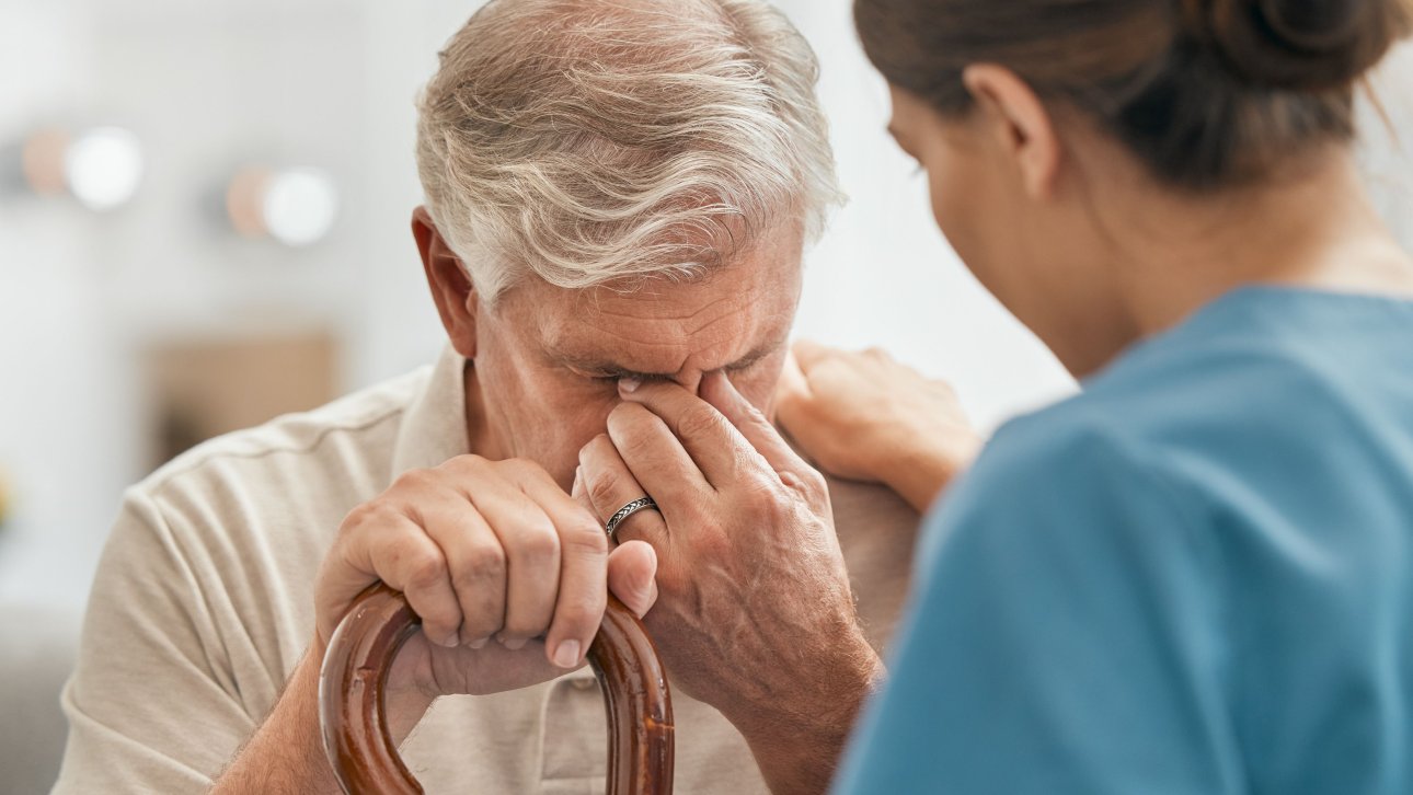 An old man holding his cane is comforted by a nurse.