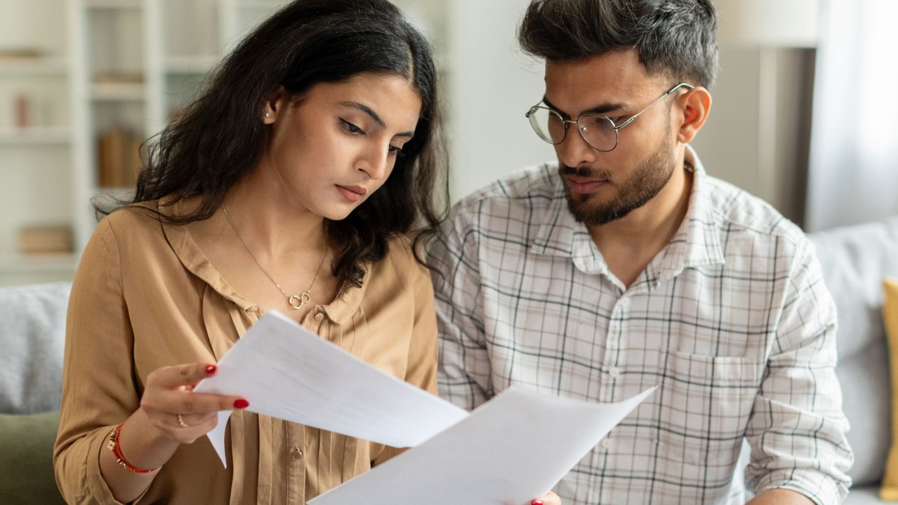 Jeune couple assis sur son divan et lisant une lettre.