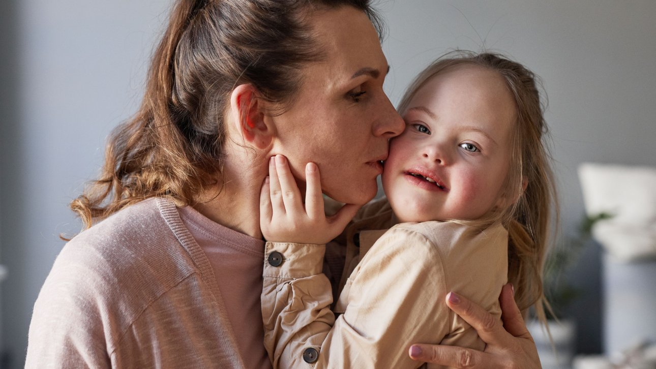 Mère embrassant sur la joue sa fillette qui a le syndrome de Dow.