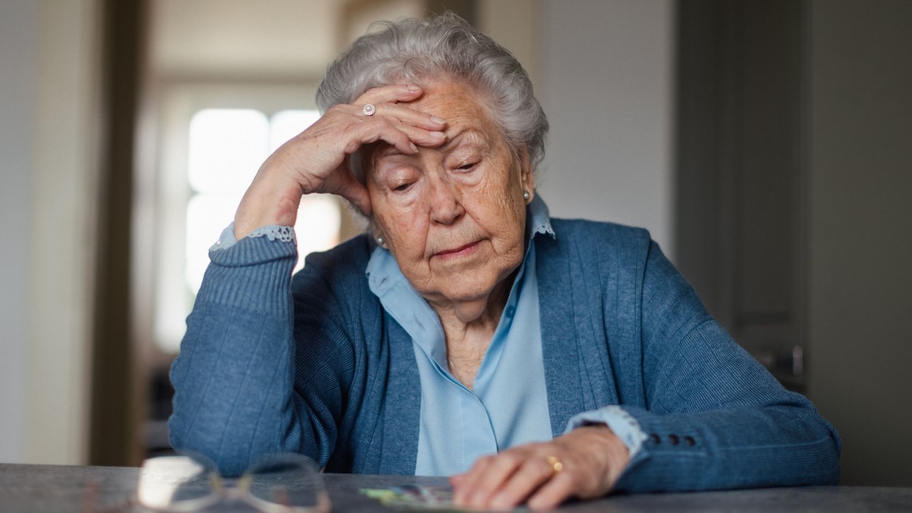 Une dame âgée regarde son argent posé sur une table en affichant un air découragé.
