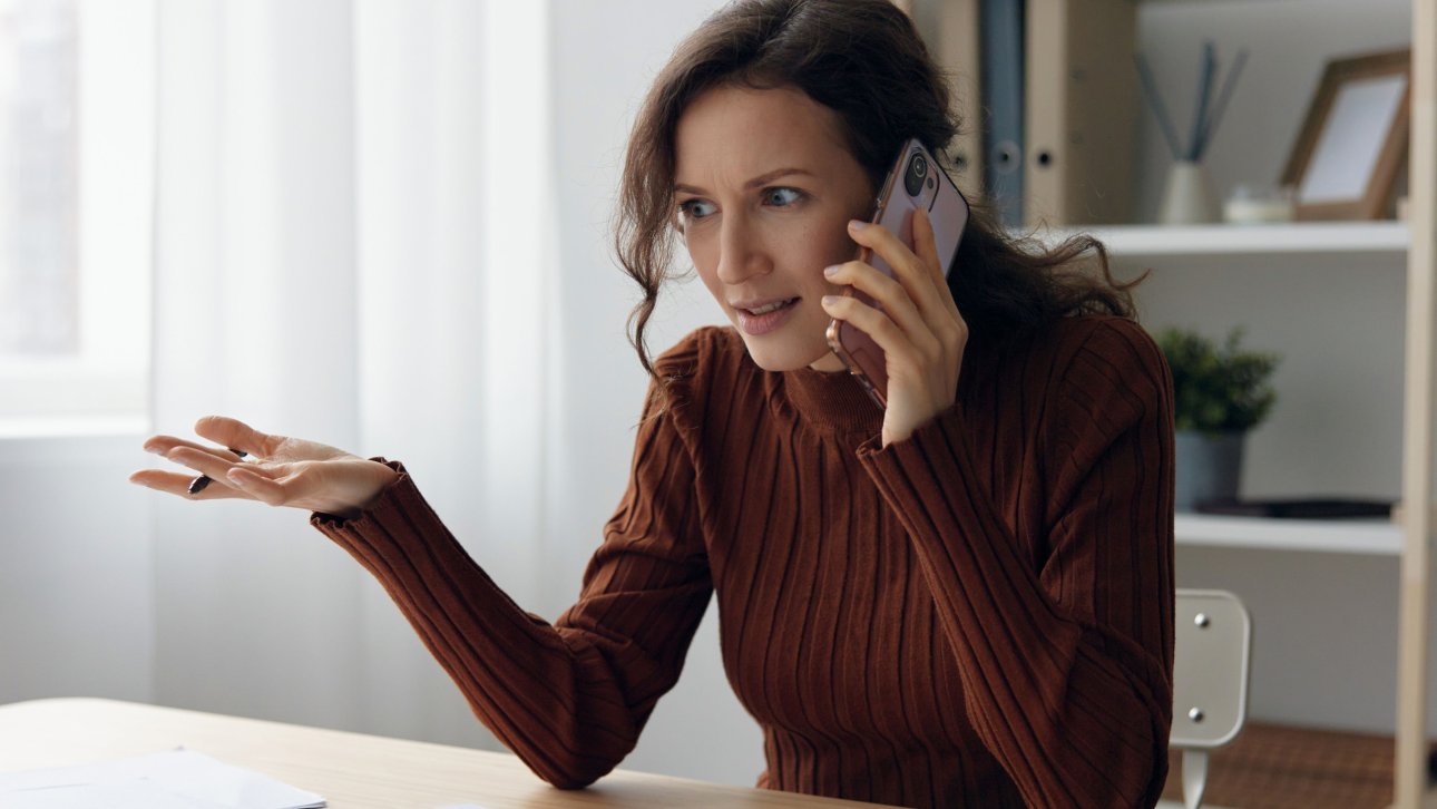 Une femme assise à une table sur laquelle des documents sont éparpillés a une discussion sérieuse au téléphone.