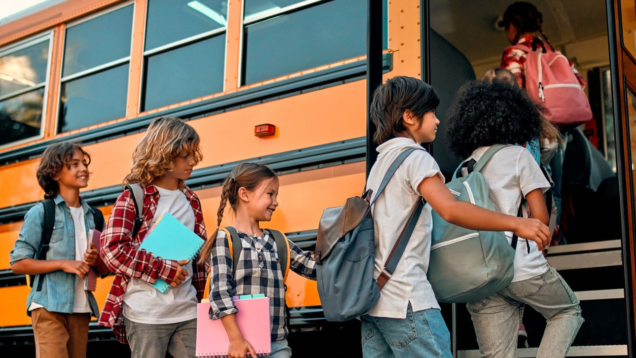 Children lining up and getting ready to board a school bus.
