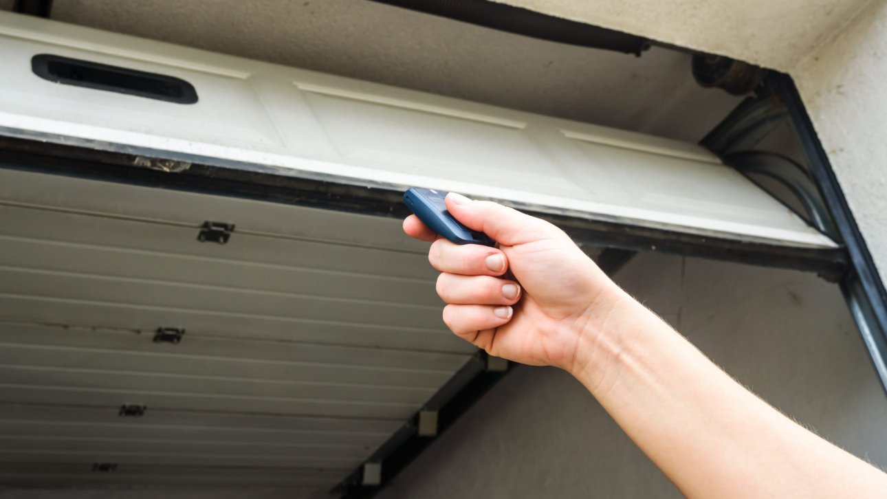 Hand holding a remote control in front of an open garage door.