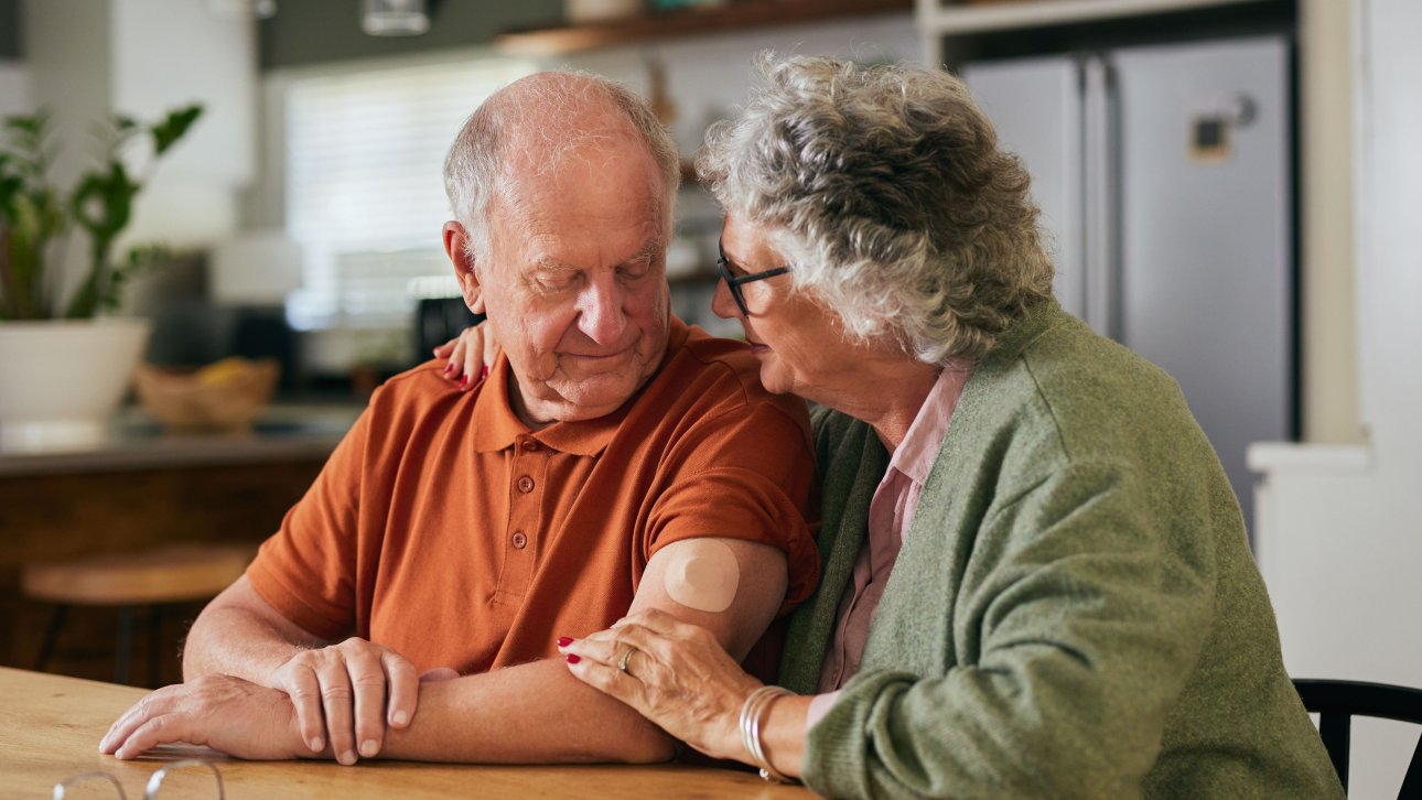 Une femme âgée touche le bras de son conjoint avec tendresse à la table de la cuisine.