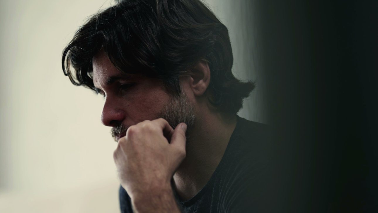 Visage d'un homme pensif dans une pièce sombre.